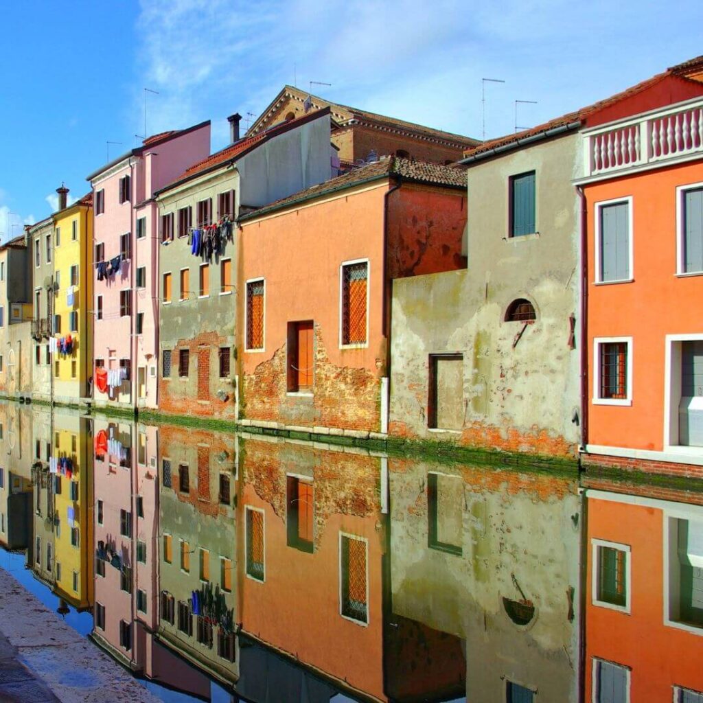 Colorful buildings in Chioggia Italy. The buildings stand along a canal, and are reflected in the still water below.