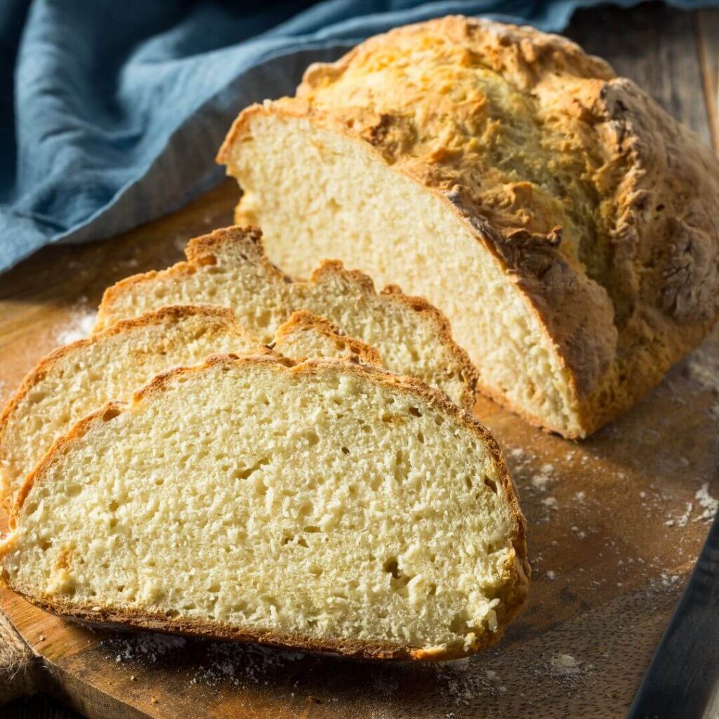 Close up image of a cut loaf of Irish soda bread on a cutting board with three cut slices laying in front of the remaining loaf, showing the bread's delicate crumb