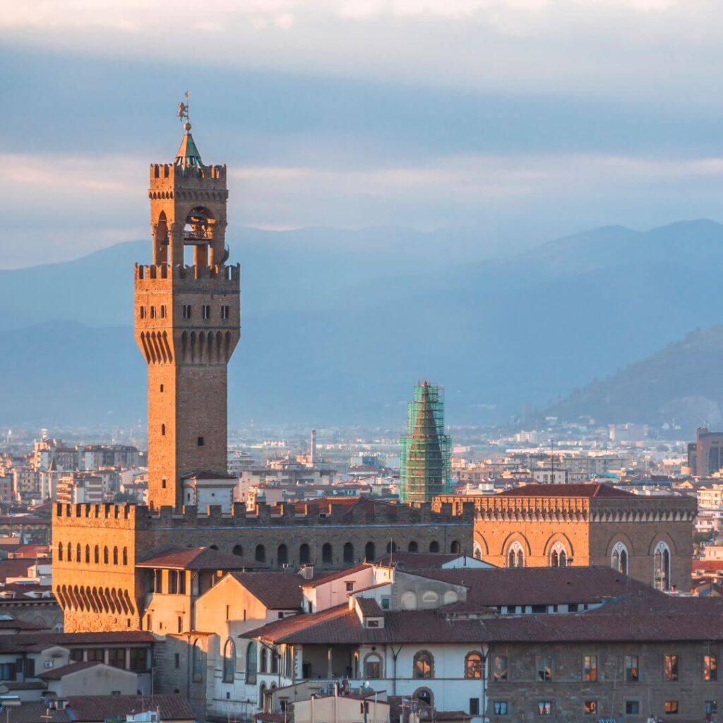 The tower of the Palazzo Vecchio in Florence, Italy. The tower stands above the city, with mountains in the background and the light at sunrise making the tower almost glow.