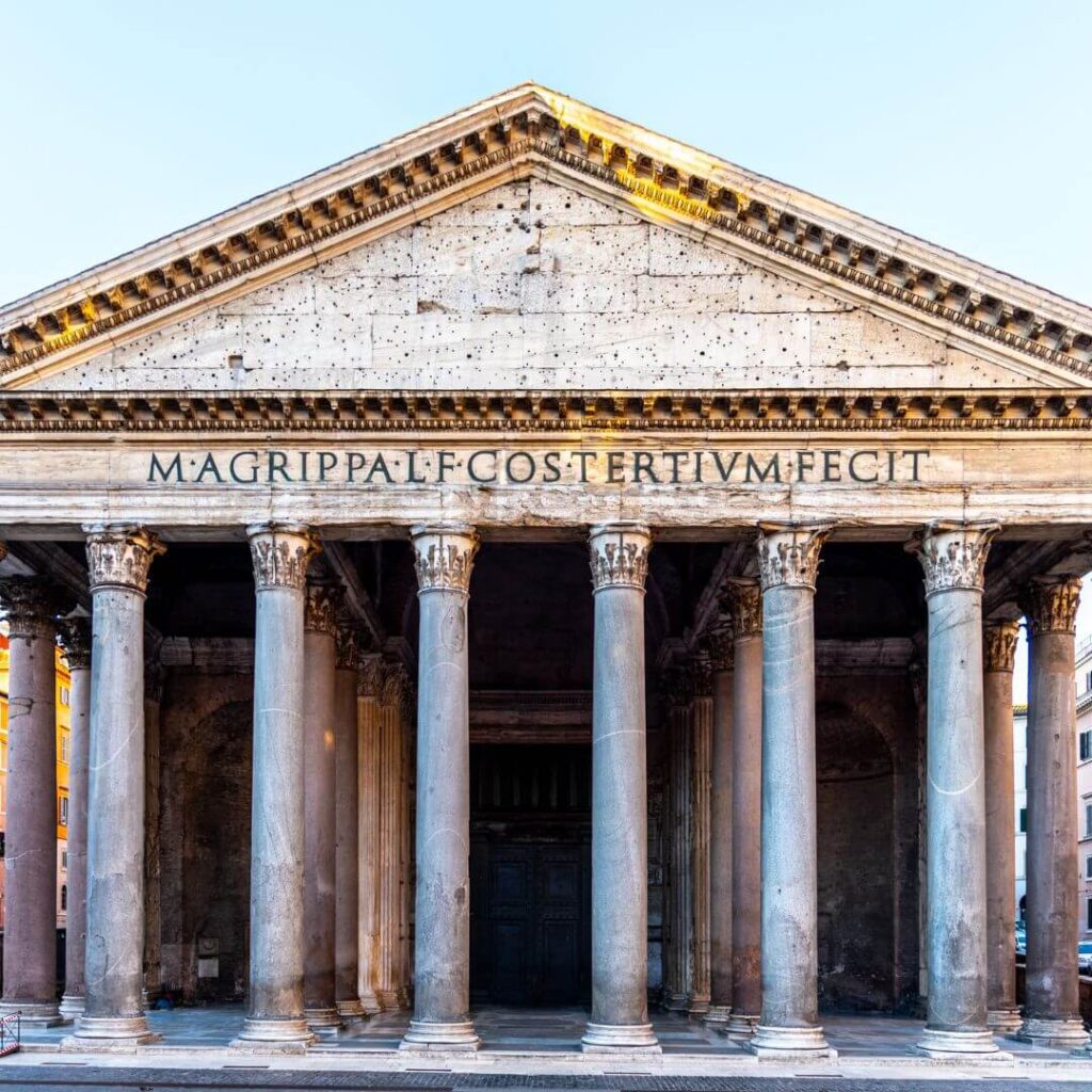 An exterior of the Pantheon in Rome Italy, with the ancient columns flanking the entrance and an inscription over them.
