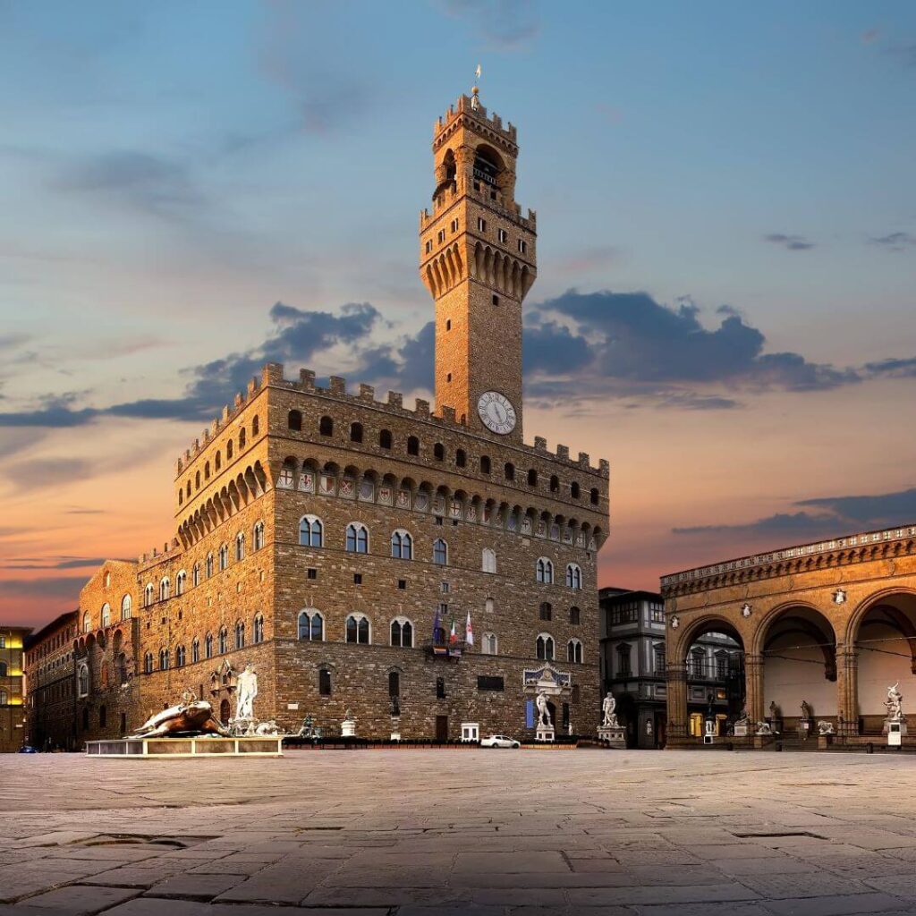 The Piazza della Signoria, with the Loggia dei Lanzi and the Fountain of Neptune. The piazza is nearly empty at sunrise, with the sky in pink and orange behind the tower of the Palazzo Vecchio.