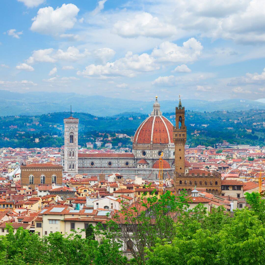 Santa Maria del Fiore, the Duomo of Florence, with the tower of the Palazzo Vecchio and Giotto's Belltower. The structures tower over the city, with the hills that surround the city in the background.