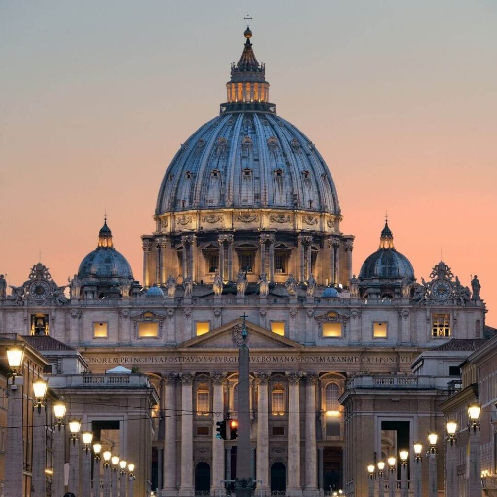 The front of St. Peter's Basilica and the dome, designed by Michelangelo, at dusk. The darkening sky behind the dome is turning pink.