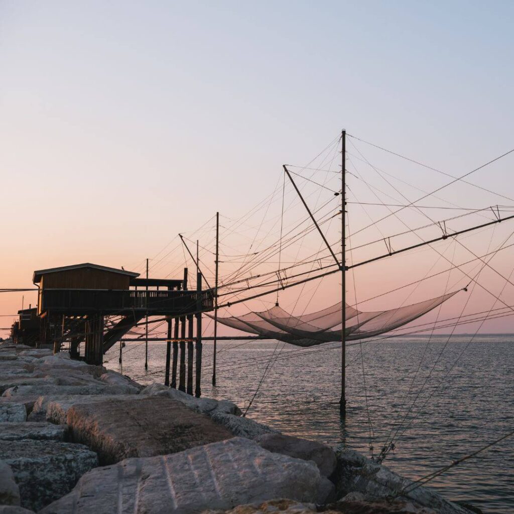 A fisherman's hut built on the rocks near Chioggia Italy. The nets are suspended on a complex network of poles and lines over the water. It's sunset and the sky is turning shades of pink and purple.