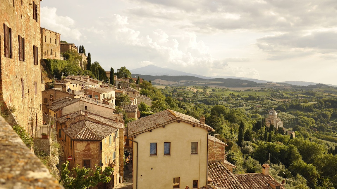 Sienna-colored houses overlooking the green Tuscan countryside