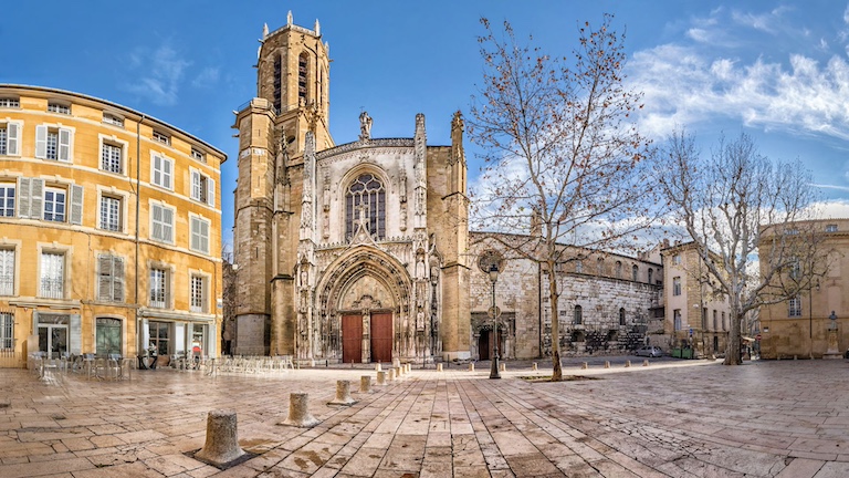 The front of the Aix cathedral across a cobbled square framed against a bright blue sky