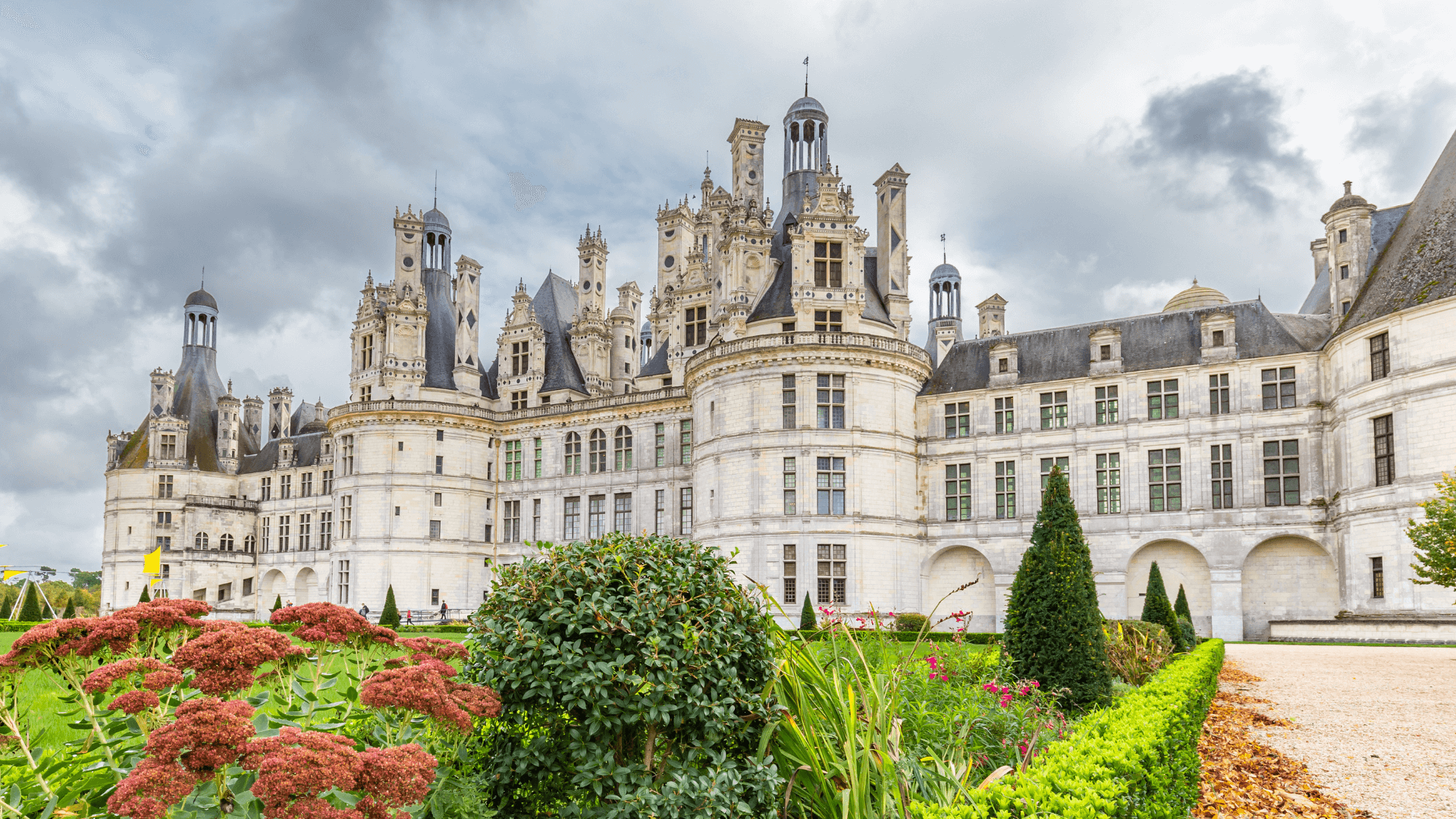 Looking up at Château de Chambord against a grey cloudy sky with greenery in the foreground