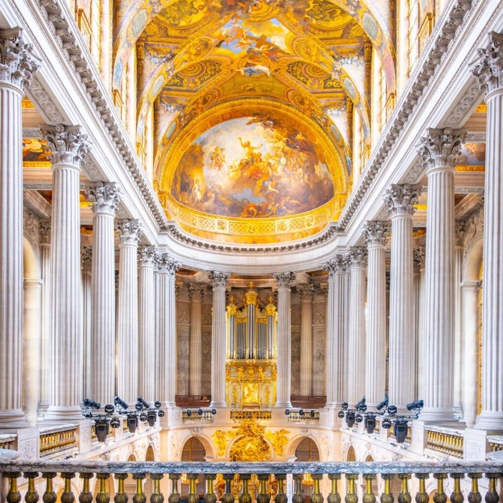 The upper level of the chapel at Versailles with elaborately painted ceilings and white marble columns