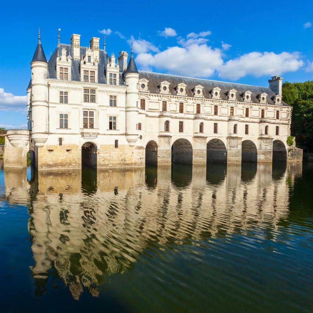 Chateau de Chenonceau, one of the best known Loire Valley castles, with it's arches spanning the Cher River and the castle and blue sky above reflecting in the calm water