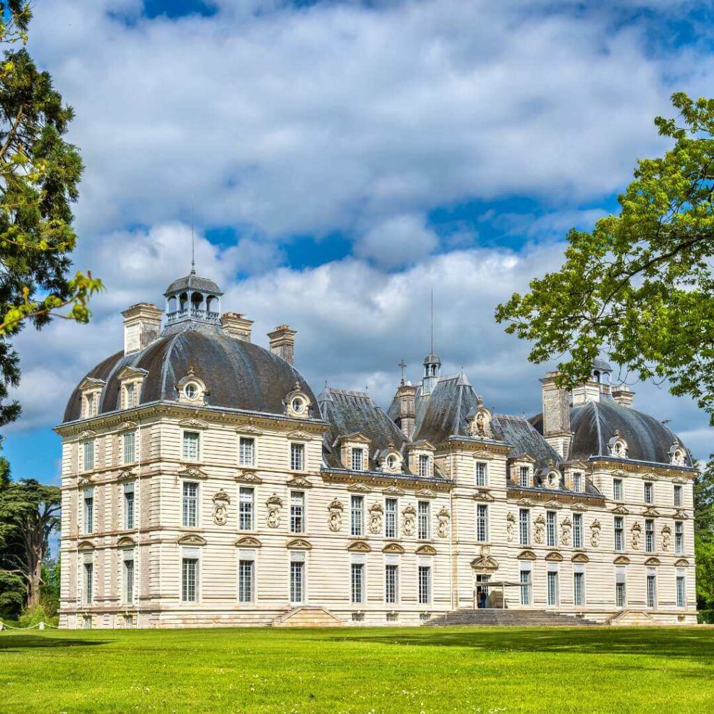 Exterior view of Chateau de Cheverny against a blue sky filled with white puffy clouds and the edge of trees in the foreground