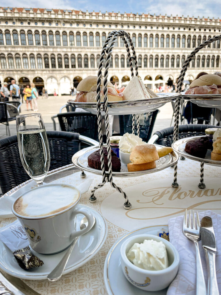 Brunch and cappuccino  with food served on 2-tier cake stands at tables alongside the Piazza San Marco