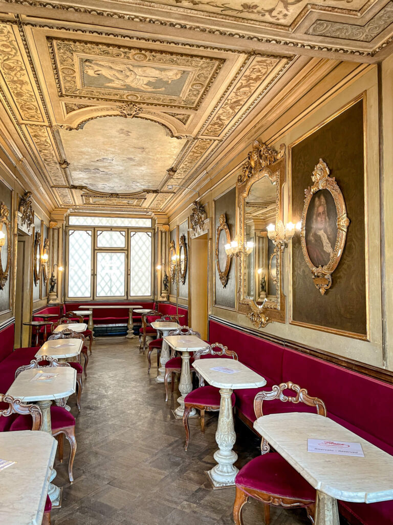 White tables, red velvet benches and gold framed ceilings in the interior of Caffe Florian on the Piazza San Marco