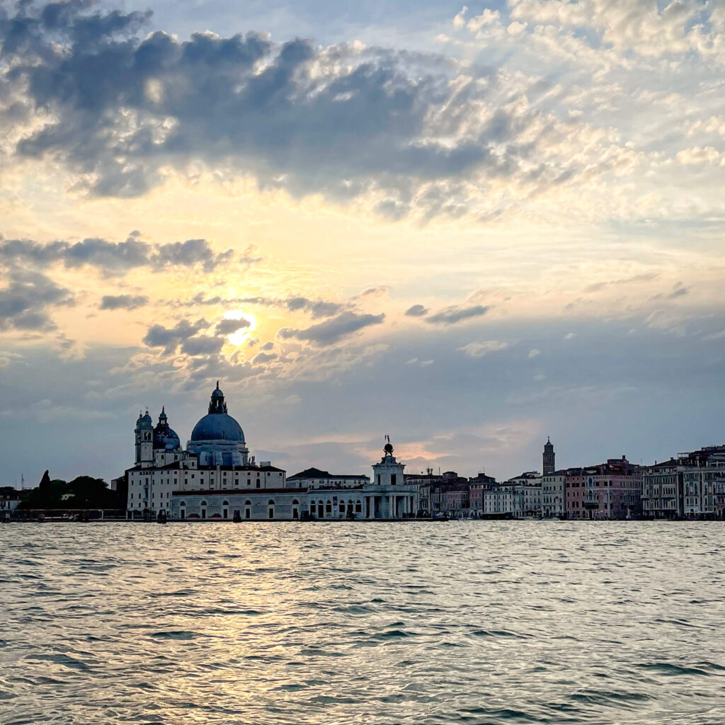 View from the water as the sun is setting with Venetian buildings silhouetted against the sky on our Venice Italy trip