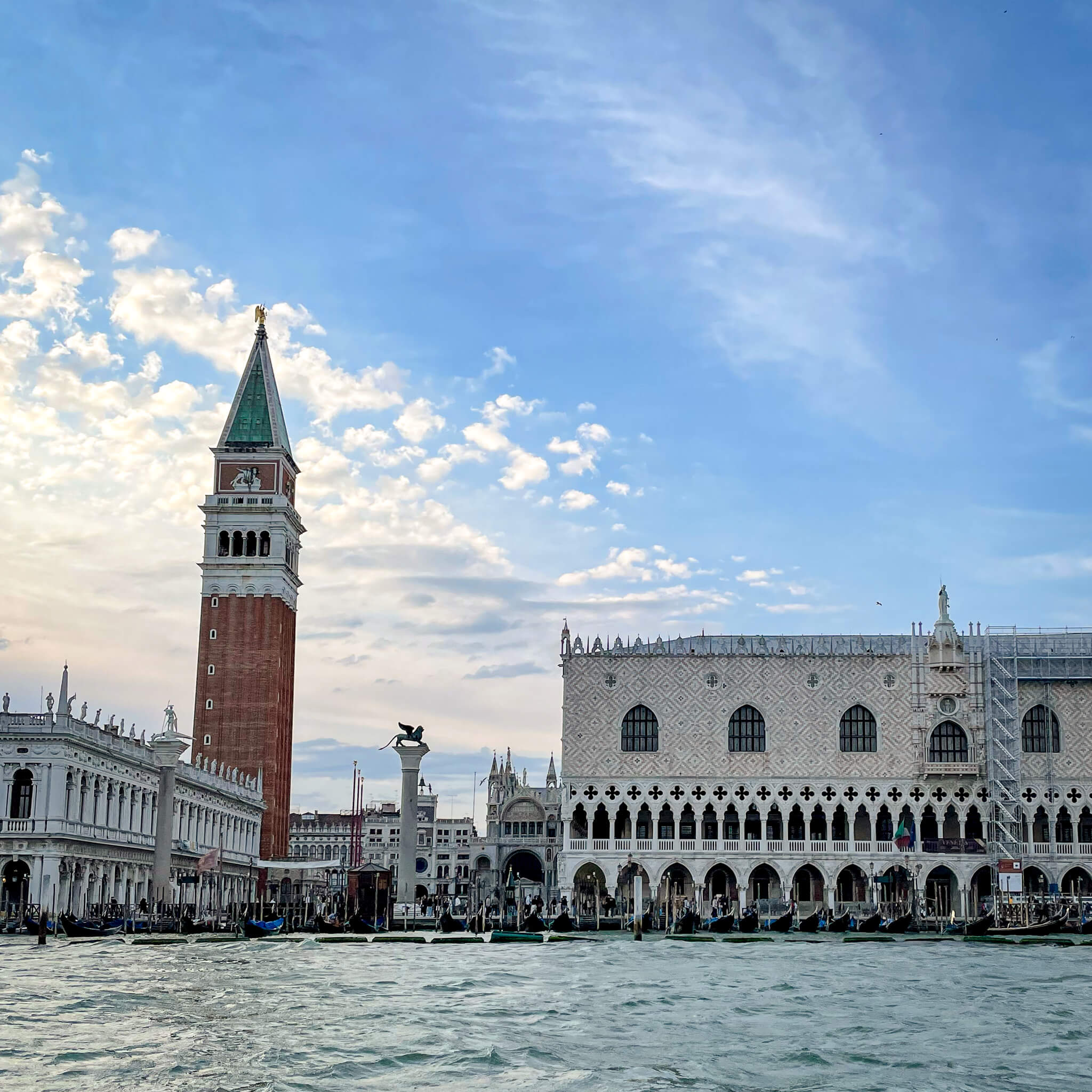 View from the lagoon, looking across the water at the side of San Marco and the belltower in the Piazza San Marco with gondolas lined up along the edge of the lagoon