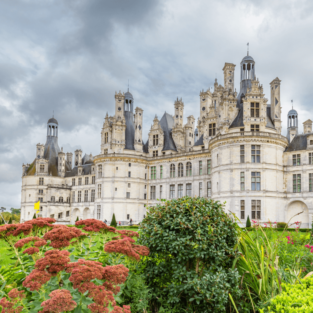 Looking up at Château de Chambord against a grey cloudy sky with greenery in the foreground