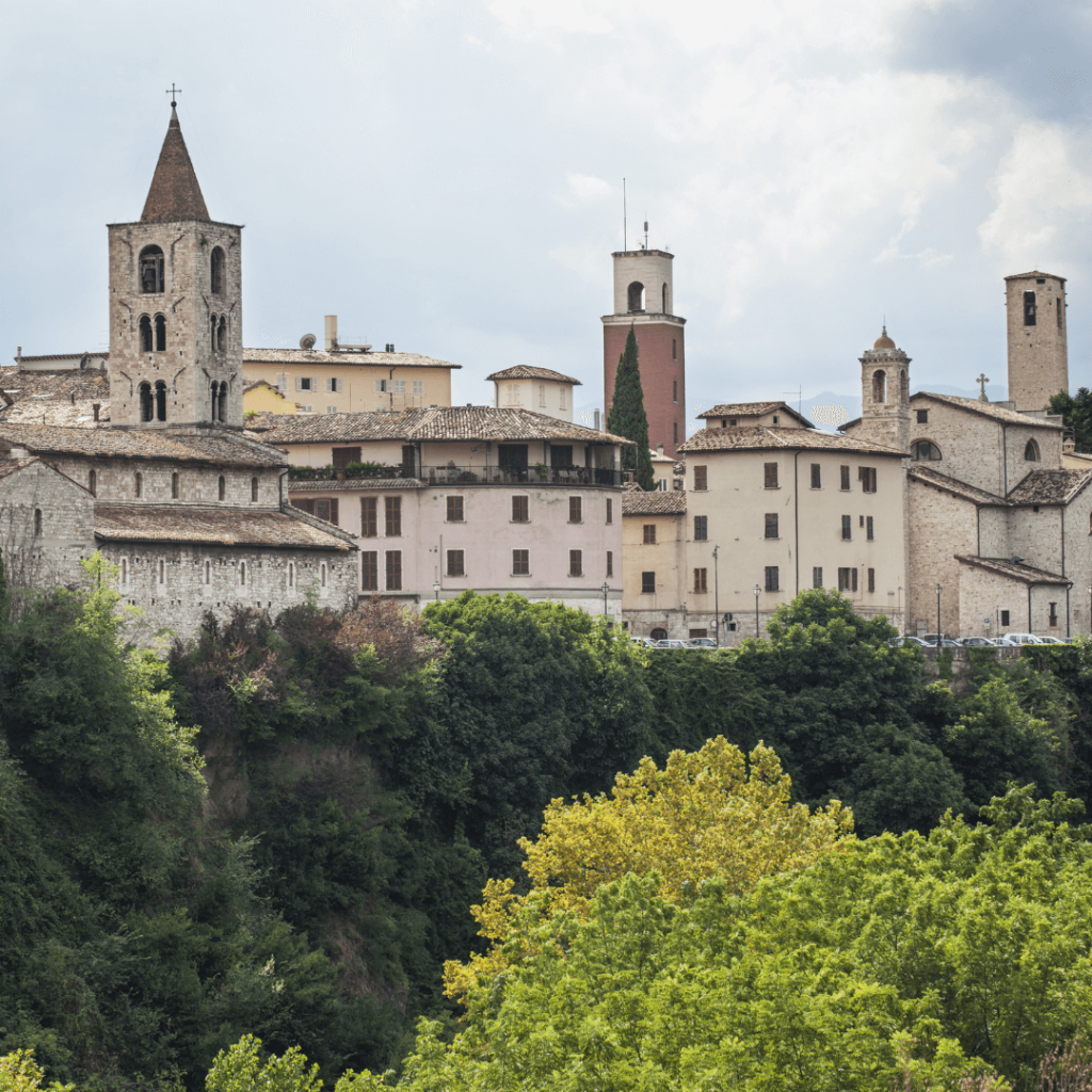 The tan stone buildings of Ascoli Piceno rising above the tops of green leafy trees