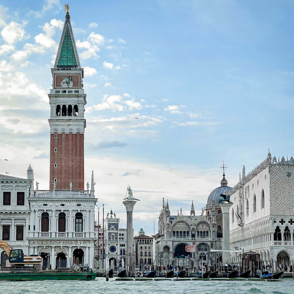 The belltower and Piazza San Marco silhouetted against a blue sky as seen from the water in the Venetian lagoon