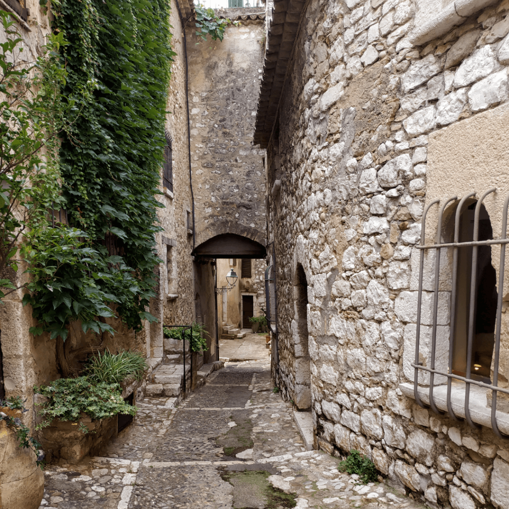 View of stone buildings with old bars over the windows down an alleyway in Saint Paul de Vence