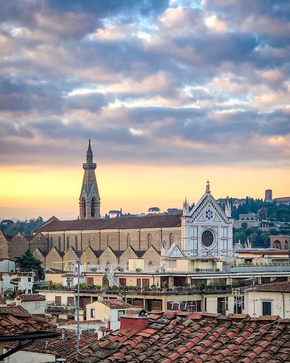 Looking across the rooftops of Florence neighborhoods with the Church of Santa Croce silhouetted against the cloud filled blue sky as the sun is going down.