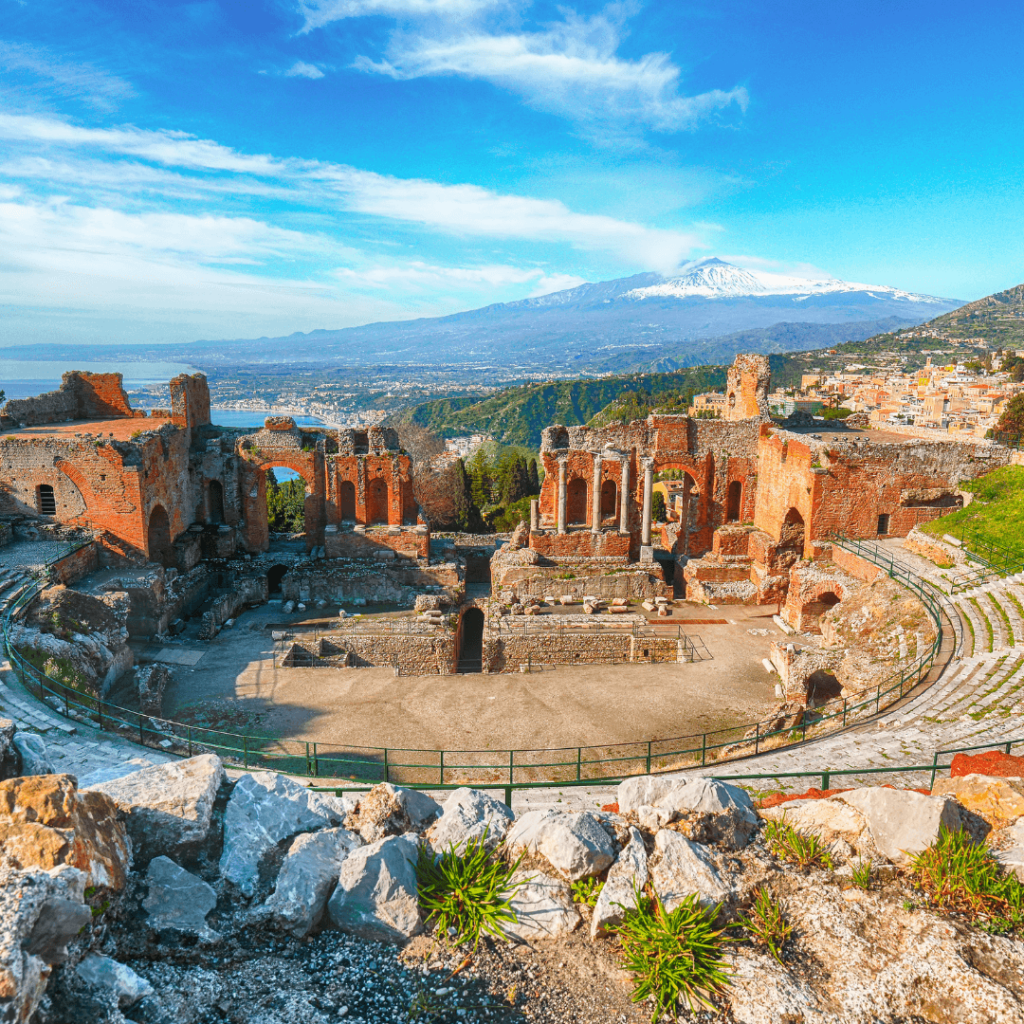 The red stone ruins and curved stone walls of a greek amphitheater against a bright blue sky