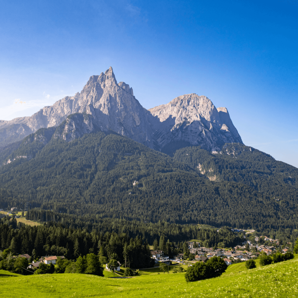 Towering rocky mountains rising from green tree-covered hills and fields of green grass