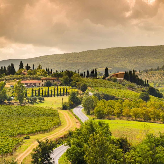 Overlooking the Tuscan countryside with sharp cypress trees and rolling green and yellow hills under a cloudy sky in Autumn, the best time to visit Tuscany Italy