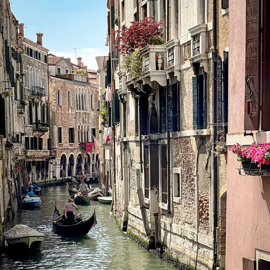 Venetian canal with gondolas floating between the buildings and potted flowering plants hanging over canal-side balconies